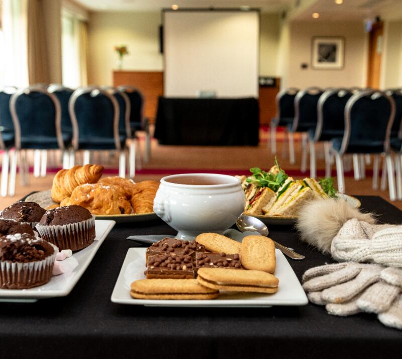 meeting room with chairs, table with muffins, pastries, soup, biscuits sandwiches and a hat and scarf