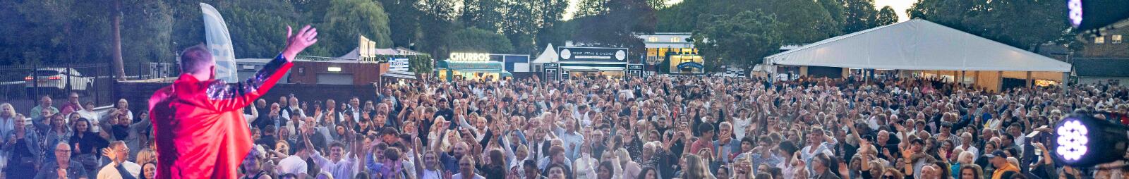 A live performer sings to a crowd at sunset at Windsor Racecourse