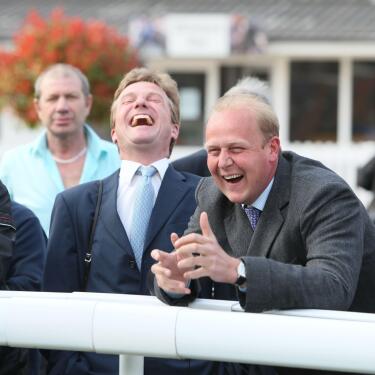 Two race goers in suits laughing at the track side at Windsor Racecourse.