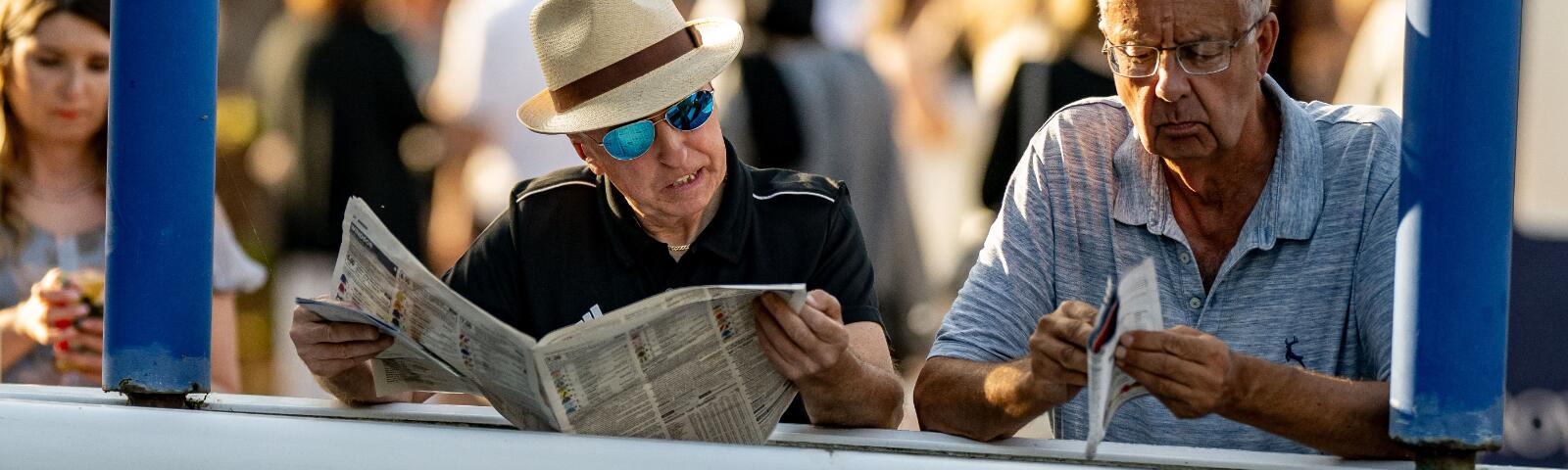 Two gentlemen reading the race card and racing post at the parade ring at Windsor