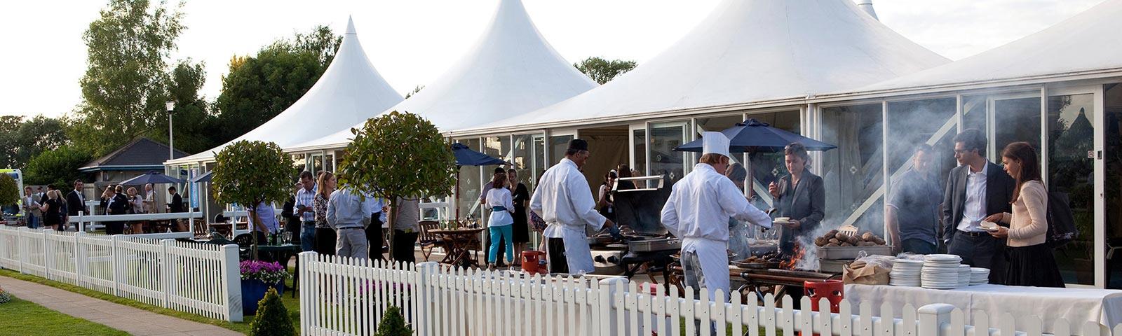 Chefs cooking in the great outdoors with diners gathering around.
