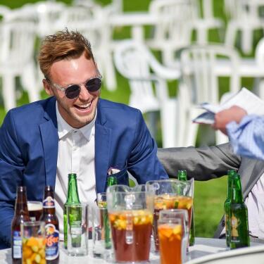 A male race goer in a suit laughing with friends at Windsor Races.