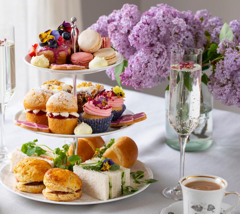 afternoon tea on a tiered cake stand, with a cup of tea and two glasses of champagne