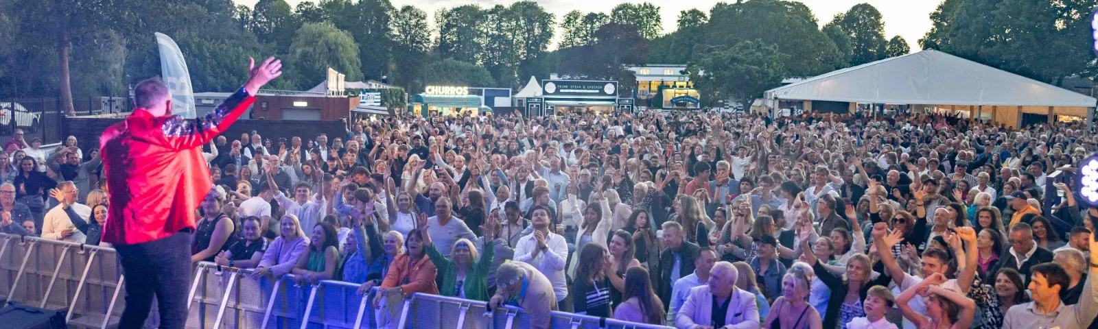 A live performer sings to a crowd at sunset at Windsor Racecourse